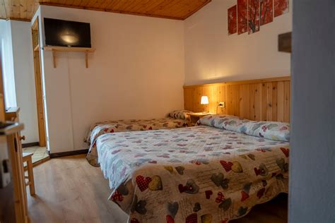 Interno di una camera dell'Hotel Club Funivia con letto confortevole, TV a schermo piatto e balcone con vista sulle montagne.