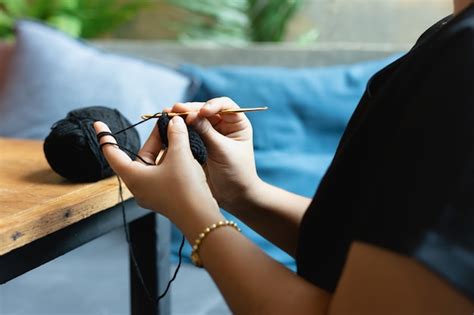 Primo piano delle mani che lavorano all'uncinetto, focalizzato sulla creazione del pollice di una muffola