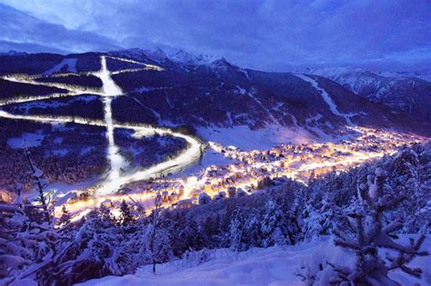 panoramica notturna di una pista da sci illuminata tra le montagne innevate