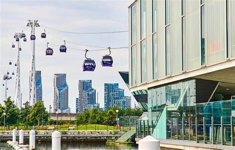 Vista aerea di Londra con la funivia IFS Cloud Cable Car sospesa sul Tamigi, con lo skyline di Canary Wharf sullo sfondo.