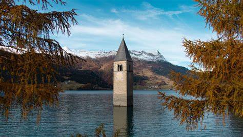 Vista panoramica del Lago di Resia con il campanile sommerso e persone che praticano sport invernali