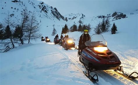 Motoslitta che trasporta persone verso una baita innevata al tramonto