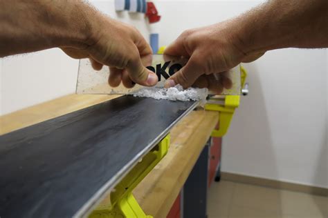 persona che raschia via la sciolina in eccesso da uno snowboard