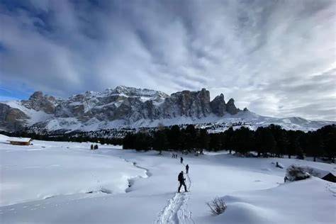 Panorama innevato delle Dolomiti, con escursionisti che camminano con le ciaspole su un sentiero.