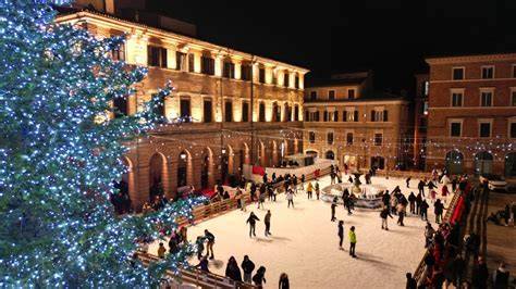 Piazza Cesare Battisti a Macerata addobbata per Natale, con la pista di pattinaggio sul ghiaccio come elemento centrale e un grande albero illuminato.