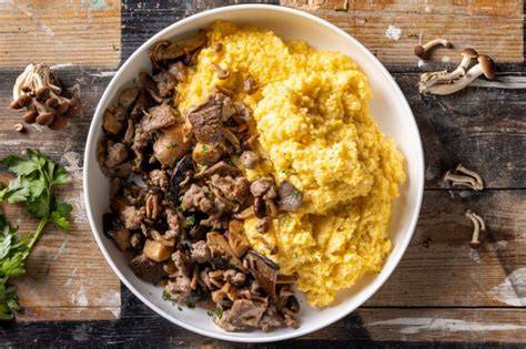 piatto di polenta concia fumante con salsiccia e funghi in un rifugio di montagna