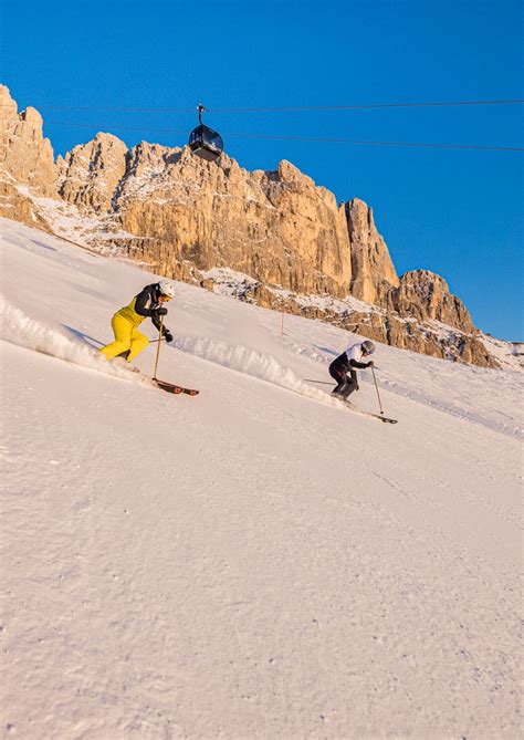 Sciatori che scendono su una pista soleggiata nella ski area Carezza