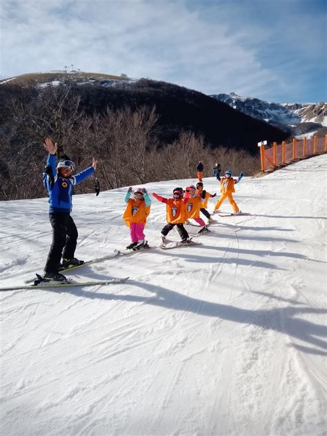 Gruppo di adulti che seguono una lezione di sci con un maestro sorridente su una pista facile.