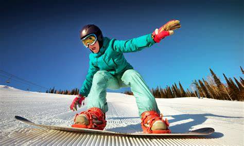 Ragazza sorridente con attrezzatura da snowboard colorata, sullo sfondo una pista innevata