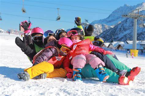 Maestri di sci e snowboard che insegnano a bambini su una pista innevata.