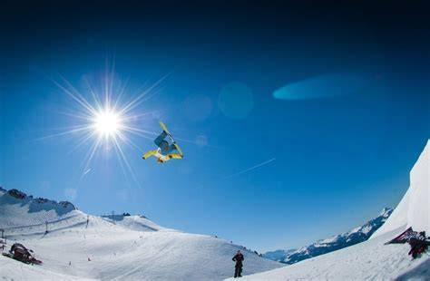 Atleta di snowboard in azione nell'halfpipe, con la neve che schizza ai lati della rampa.