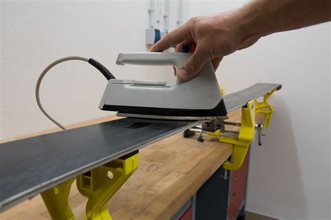 Primo piano di un ferro da sciolinatura che fa sciogliere un blocco di sciolina sulla base di uno sci.