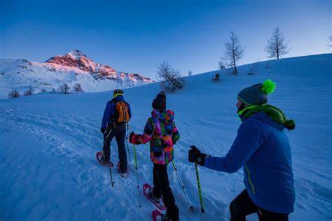 Bambini che fanno ciaspolate al tramonto in un paesaggio innevato.