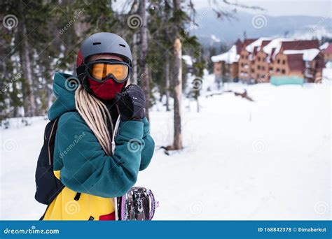 Una giovane donna, Kim, con uno snowboard, guarda pensierosa verso un campo da gara innevato, con le montagne sullo sfondo.